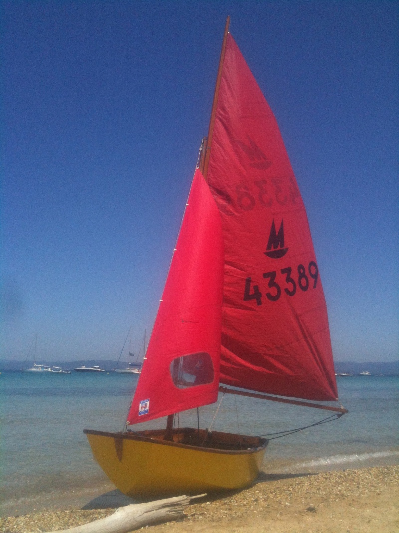 'Les Oiseax' on a sunny beach on the island of Porquerolles A yellow Mirror dinghy on a beach with cloudless blue sky and transparent blue water